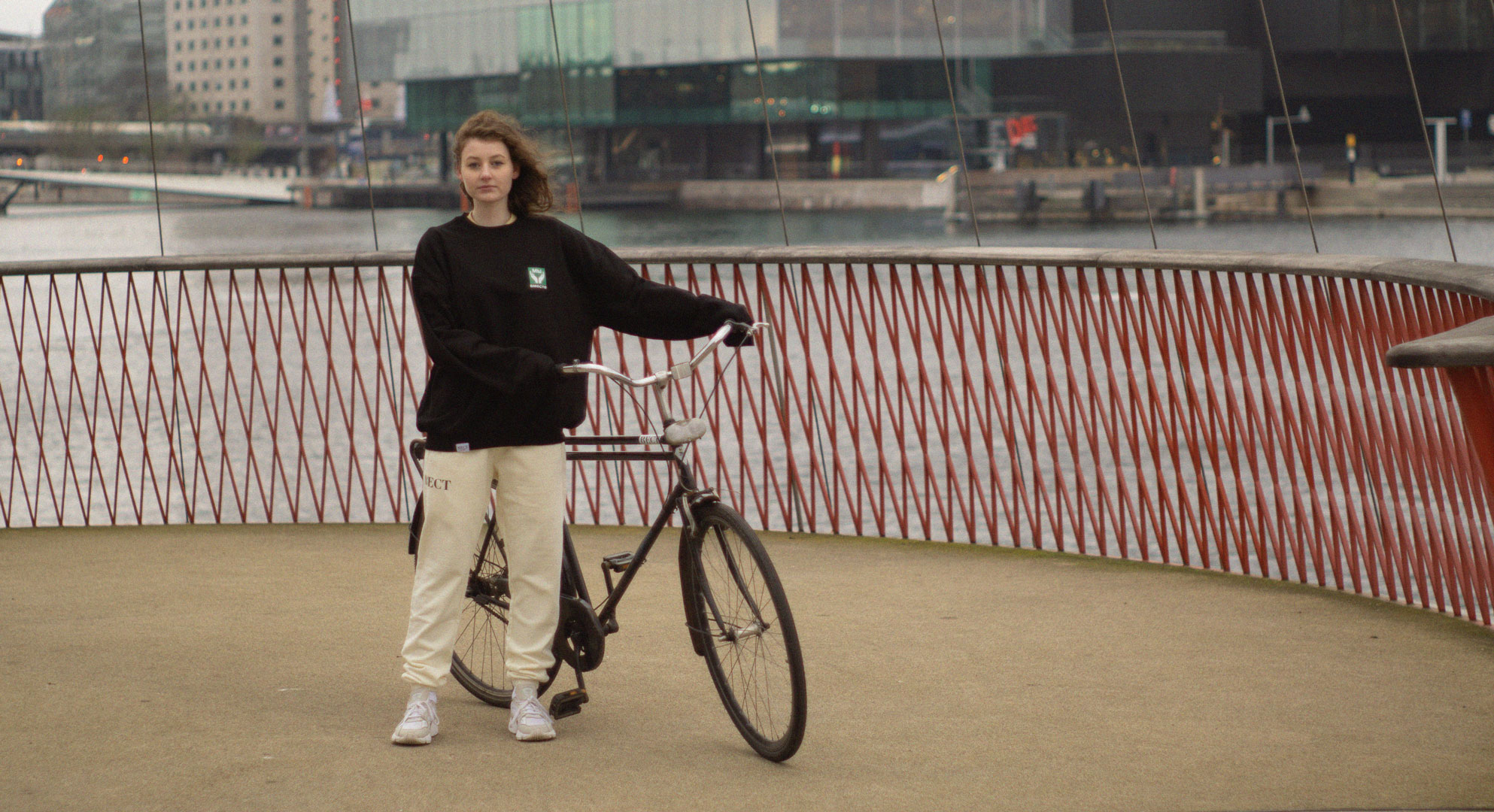 Female Model with BECT We Are Together Sweater holding bike at Circle Bridge in Copenhagen, Denmark