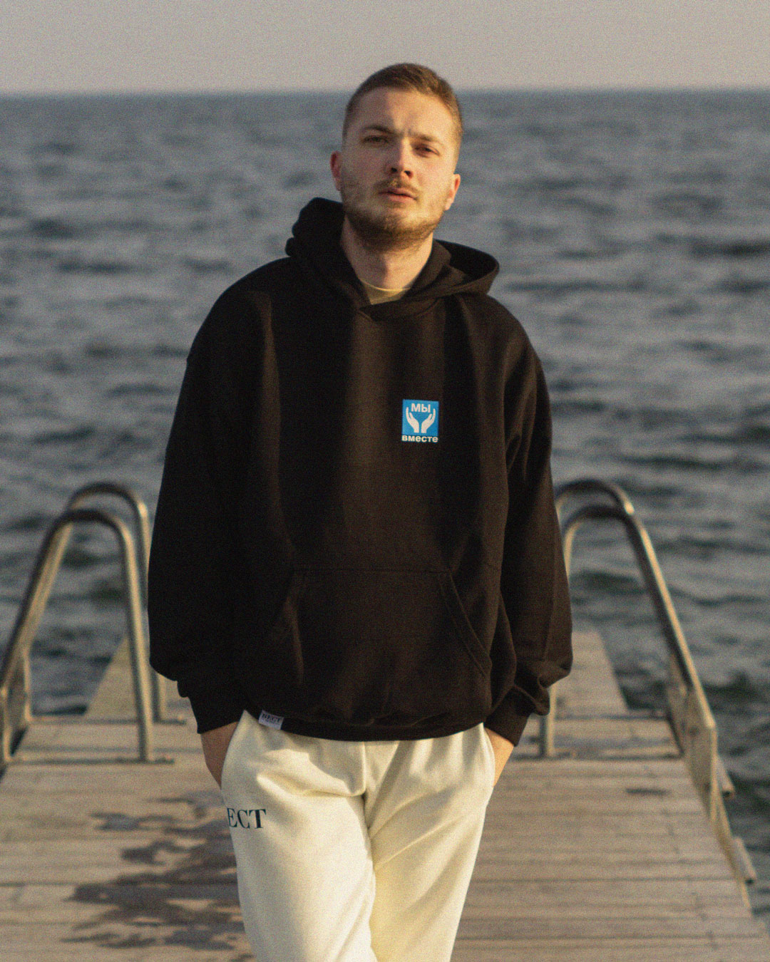 Male Model with BECT We Are Together Hoodie at Amager beach in Copenhagen, Denkmark, with the ocean in the background